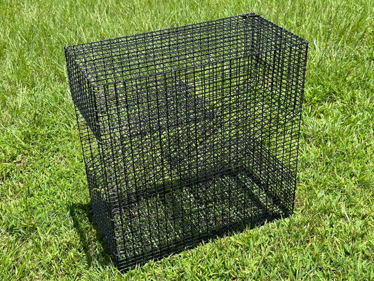 A black wire mesh rectangular cage or pinfish trap placed on green grass outdoors.