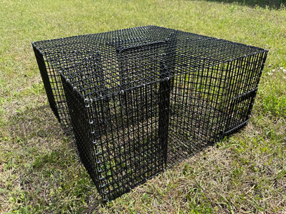 A black PVC-coated wire mesh pinfish trap or enclosure box placed on a grassy outdoor lawn.