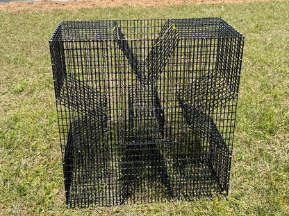 A black metal wire mesh cloverleaf style fish trap or enclosure with a slotted wire design, photographed outdoors on a grassy lawn.