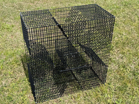 A black PVC-coated cloverleaf pinfish or baitfish trap sitting on a grassy lawn. 
